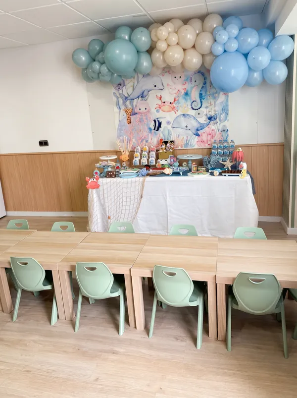 Mesa dulce con decoración marina, globos y mesas infantiles preparadas para un cumpleaños
